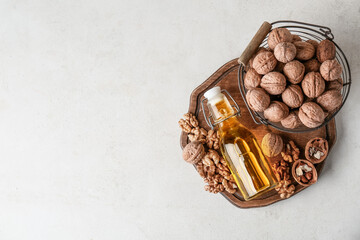 Bottle of fresh walnut oil and basket with nuts on white background