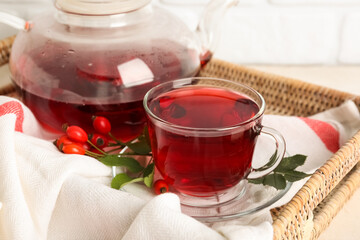 Glass cup and teapot of hot rose hip tea on white table, closeup