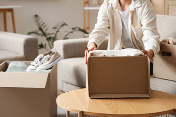 Young woman unpacking cardboard boxes with new clothes and sneakers on sofa in living room, closeup