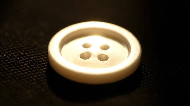 Illuminated white button with four holes on a dark fabric surface