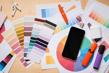 Mobile phone with earphones, stationery and color palettes on brown wooden background, top view