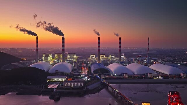 Industrial landscape of a thermal power plant with smoke stacks emitting smoke at sunset