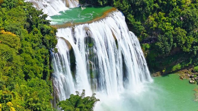Aerial view of majestic Huangguoshu Waterfall cascading into an emerald pool surrounded by lush forest, Guizhou, China.