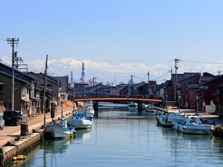 Scenic landscape of Shinminato Uchikawa canal and fishing boats under the snowy Tateyama Mountains in Toyama Prefecture, Japan.