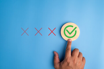 Hand selecting green check mark among red cross icons on blue background, representing customer satisfaction, quality approval, decision making, evaluation process and positive feedback selection
