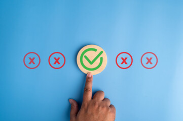 Hand selecting green check mark among red cross icons on blue background, representing customer satisfaction, quality approval, decision making, evaluation process and positive feedback selection