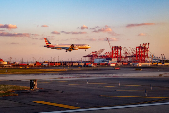 Newark Liberty Airport, Newark, New Jersey, USA - November 19, 2023 - An American Airlines Airbus 321 landing at sunset in front of the Panamax cranes of the Maher Terminals at the Port of Newark