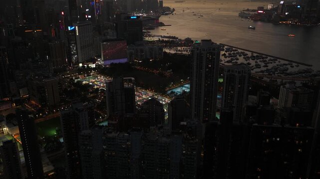 Aerial view of hong kong's illuminated cityscape and victoria harbour as morning fog rolls through the skyscrapers at sunrise, revealing the iconic urban landscape and mountains in the background