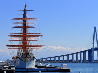 Majestic view of the tall ship Kaiwo Maru and Shinminato Bridge against the snowy Tateyama Mountains in Toyama, Japan.
