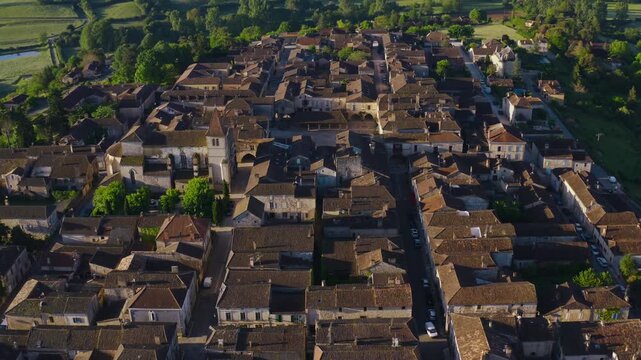 Historic houses and church tower of Monpazier village seen from above during golden hour. Wide aerial landscape view.