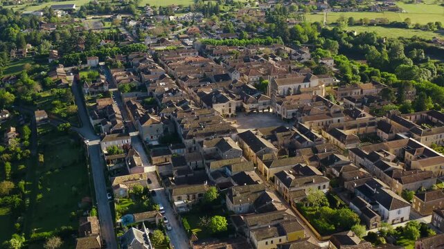 Overview of the medieval bastide of Monpazier nestled among green trees and fields in Dordogne. Wide aerial shot.