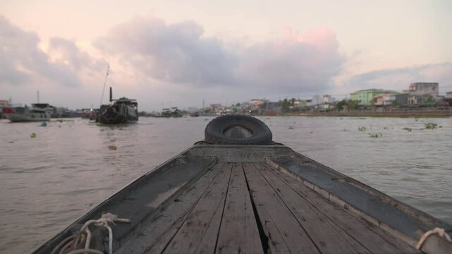 Dawn Wooden Boat Mekong Delta Market Approach, Slow Glide Past Stilt Houses And Floating Stalls Under Pastel Sky, Quiet Water, Weathered Deck And Rope In Foreground, Authentic Riverside