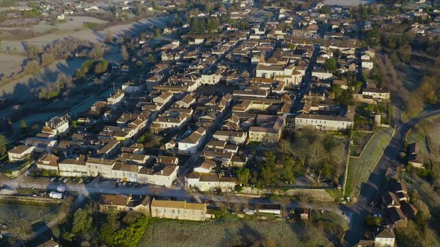 Grid layout and ancient stone buildings of the Monpazier bastide in the French countryside shown from a drone perspective.