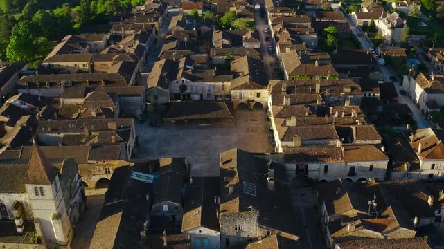 Old tiled roofs and the main marketplace of the historic town of Monpazier at sunset filmed from an aerial perspective.