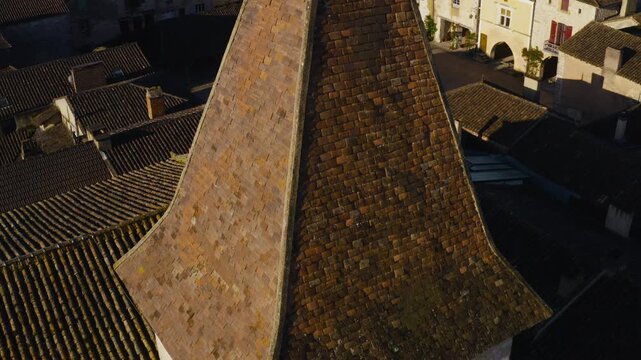 Sunlit rooftops and a church spire tower over the town square in the bastide of Monpazier, Dordogne. Drone shot focusing on architecture.