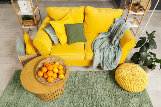 Wicker plate with citruses on coffee table near yellow sofa in stylish living room
