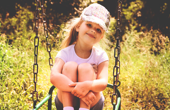 Happy child girl swinging on swings and playing on playground , summertime. Enjoying activities on playground, leisure time outdoors. Toned effect, retro
