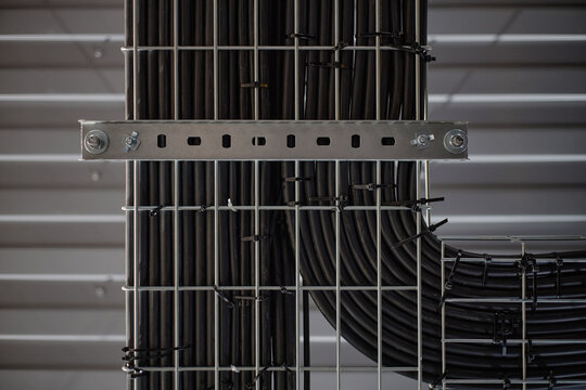 Industrial cable tray system supporting organized black electrical cables running vertically and horizontally along metal grid structure in modern facility interior