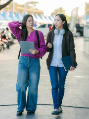 Fototapeta premium Two Asian women with active lifestyles are seen walking to work, chatting together on their way to the office.