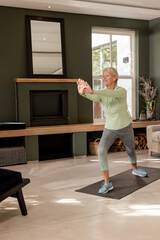 Fototapeta premium Mature adult woman performing standing lunge on black yoga mat in living room with mirror