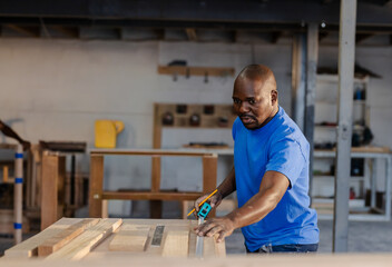 African American man in bright blue Tshirt measuring wood with tape measure in workshop, copy space © wavebreak3