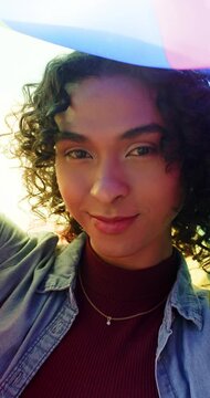 Vertical video: Non-binary adult holding translucent pastel fabric and shifting hues at warm sunset