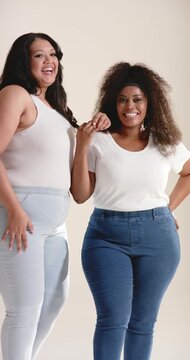 Vertical video: Diverse female friends grasping forearm and laughing while sharing joke in studio