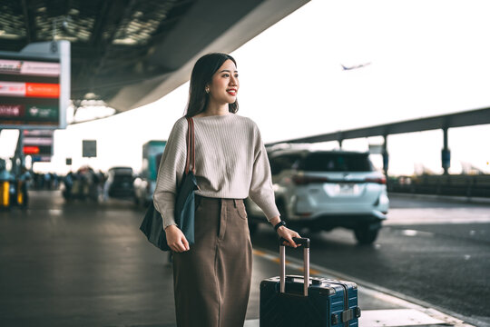 Standing asian business woman with travel luggage waiting at bus terminal for transport on day
