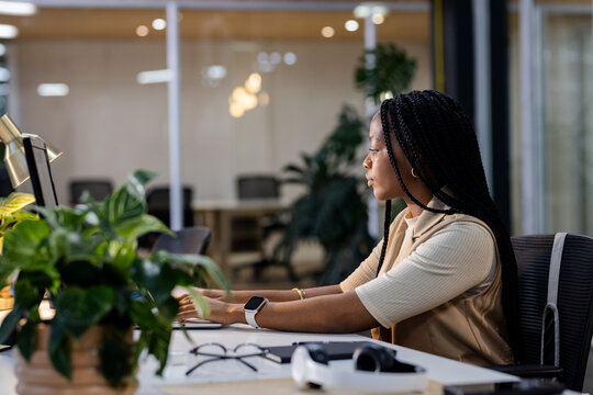 Office desk monitor and keyboard glowing under warm lamp near plant, eyeglasses by glass walls