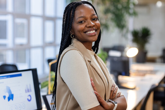 African American woman standing near desk smiling and showing smartwatch in open-plan office