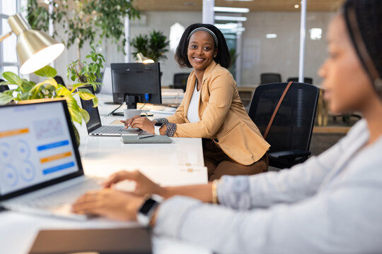 African American female coworkers typing on laptops at modern open-plan office with plants