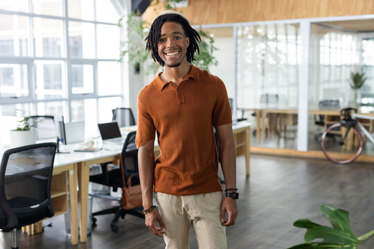 African American man in burnt orange polo shirt posing in open-plan office with laptop and bicycle