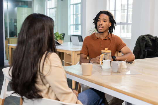 Diverse coworkers discussing project at table in coworking area with water carafe and laptop