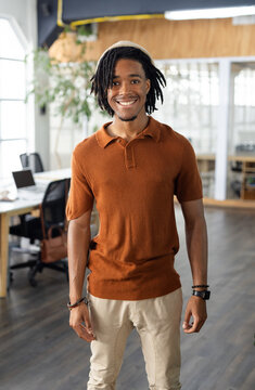African American man smiling at coworking office desk with laptop wearing brown polo shirt