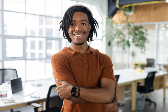 African American man standing with arms crossed in office by laptop wearing polo and smartwatch