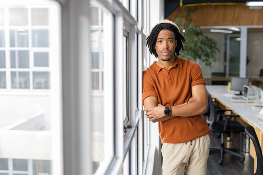 African American man leaning against window in bright office wearing knit beanie and smartwatch