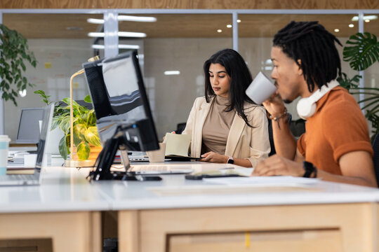 Diverse coworkers collaborating, reviewing paperwork and sipping coffee at office desk, copy space