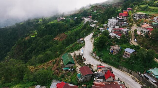 Drone flying above winding mountain road and village during rainy season