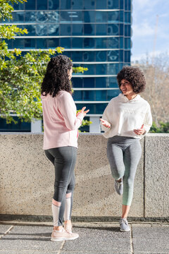 Diverse female friends in sportswear chatting and leaning on ledge on terrace