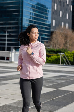 Woman in twenties jogging through tiled plaza tracking run on smartwatch, wearing running shoes