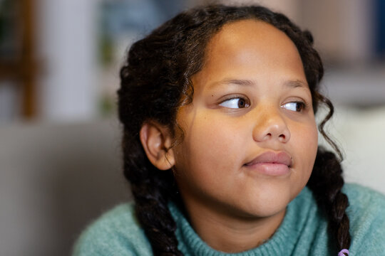 African American child sitting on couch in living room wearing teal knit sweater with braided hair