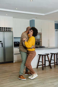 African American couple dancing and embracing in modern kitchen with stainless steel refrigerator