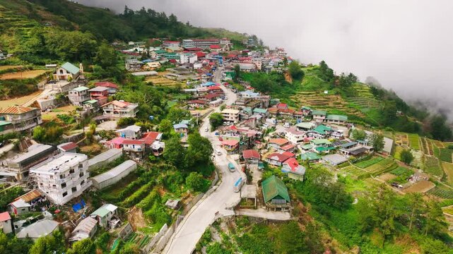 Drone gliding toward misty mountain village as sun breaks clouds in Benguet