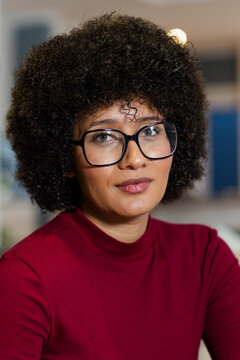 African American woman wearing red top, black-framed glasses, nose-ring facing camera in office