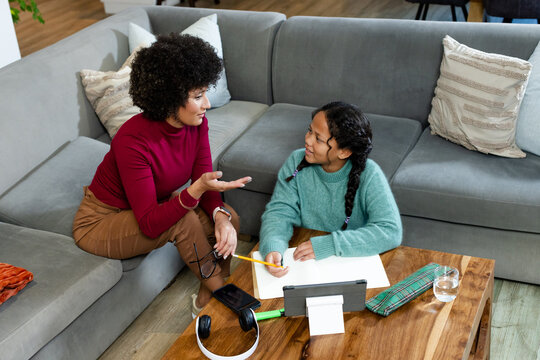 African American mother and daughter doing homework at coffee table at home with tablet and paper