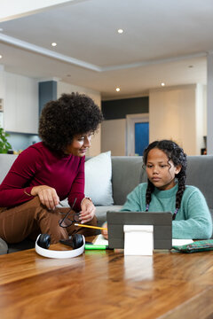 African American mother and daughter tackling homework on couch in home with tablet, copy space