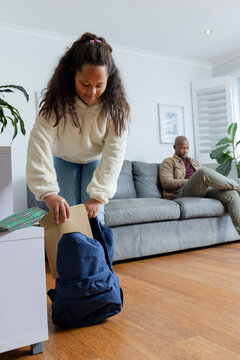 African American father and daughter checking phone, placing folder in backpack at home, copy space