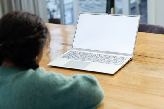 Person sitting at wooden table using silver laptop by grey curtains and sliding glass doors