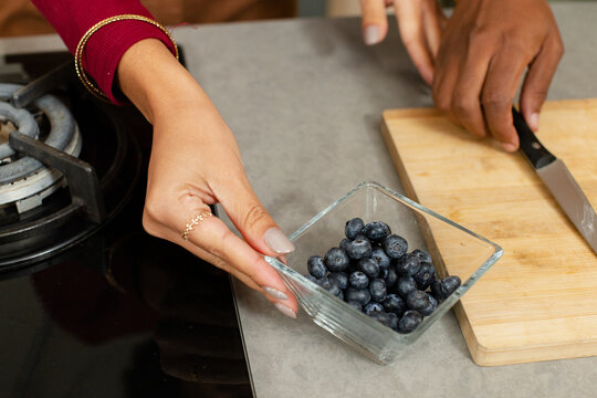 Square glass bowl is holding fresh blueberries over countertop near stove grate with chef's knife
