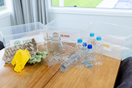 Recycling setup featuring three labeled bins with bottles and jars on wooden table beneath window